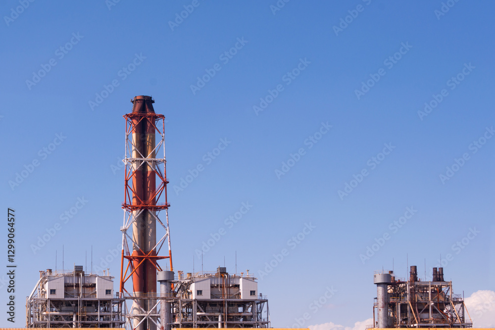 Industrial factory with smokestack against clear blue sky in daylight Industrial factory with smokestack against clear blue sky in daylight