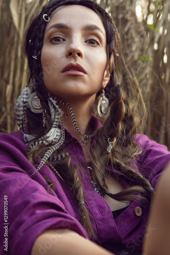 Portrait of a beautiful brunette woman in a purple dress and jewelry standing in dry bushes outside in autumn