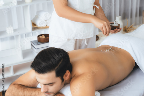 Blissful man customer having exfoliation treatment in luxury spa salon with warmth candle light ambient. Salt scrub beauty treatment in health spa body scrub. Quiescent