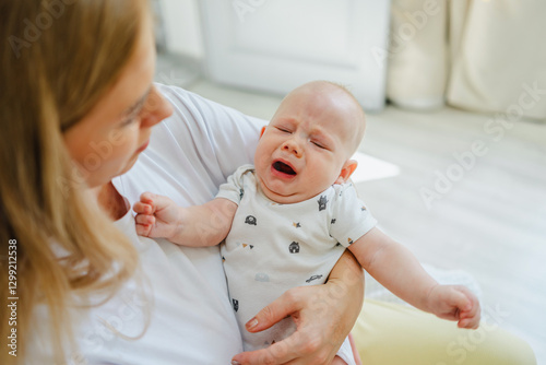 Mother comforting a crying baby in bright living room photo