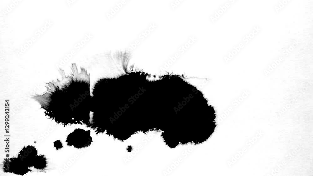Spraying black paint on a white background. Spray of ink over the white surface. Black watercolor paint spraying. Particles of black paint scatter on white paper. Close up.