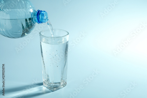 Pouring soda water from bottle into glass on light blue background, space for text
