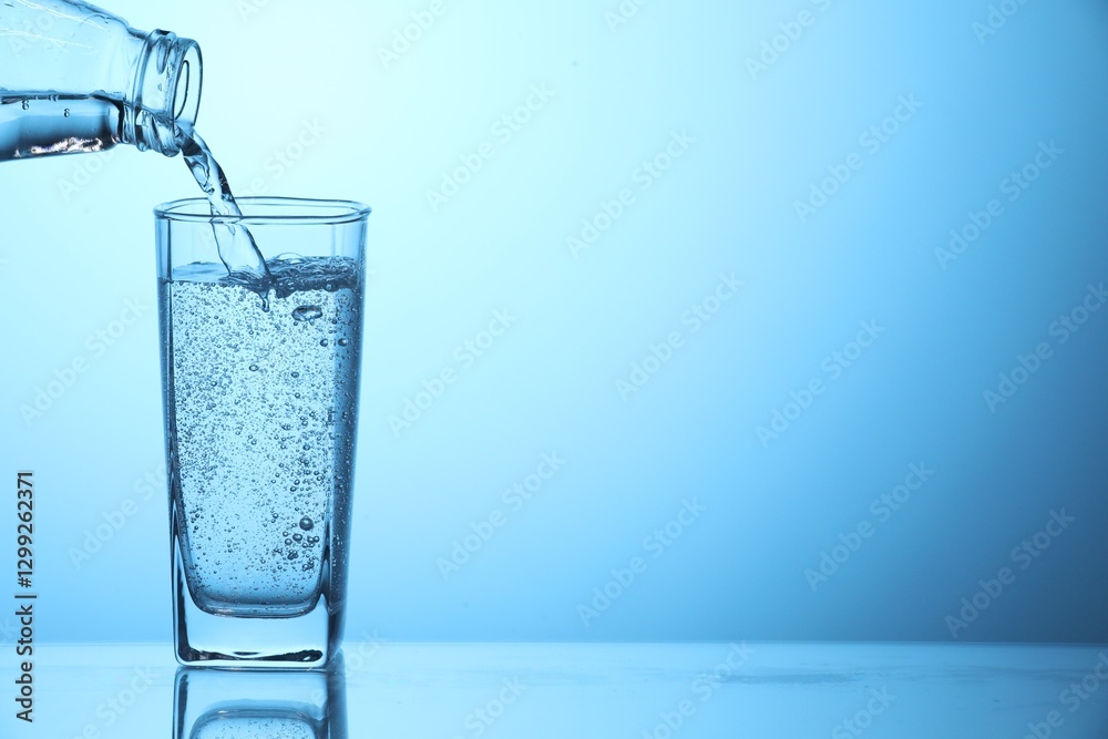 Pouring soda water from bottle into glass on light blue background, closeup. Space for text Pouring soda water from bottle into glass on light blue background, closeup. Space for text