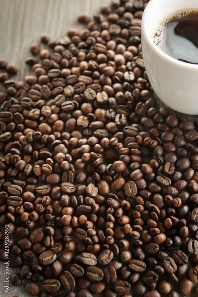 Fototapeta premium Creative arrangement of coffee beans spelling ku next to a cup of brewed coffee on a wooden surface