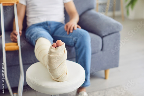 фотографія Close-up of handicapped man with leg in cast with crutch sitting on sofa at home in rehabilitation and recovering after having fractured limb