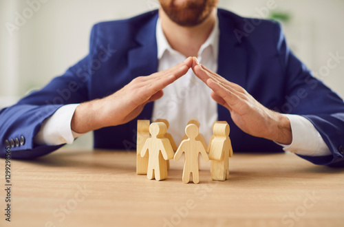 Businessman covering wooden figures of people. Employer commitment to protecting the human rights, labor rights, and providing support and insurance to employees within the community.