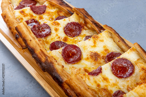 Turkish pide dish with slices of pepperoni and cheese. Turkish traditional pita. (pide with pepperoni) on wood service. Turkish name; Sucuklu pide. photo