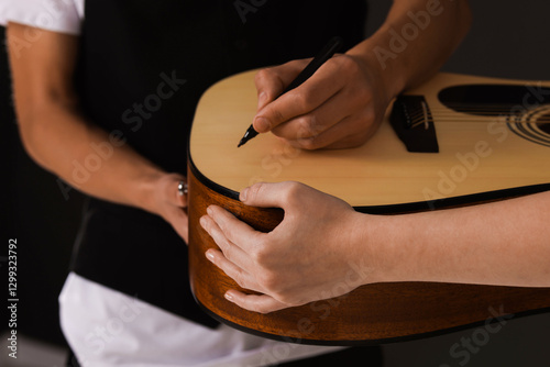 Quadro su tela Musician signing autograph on guitar against dark background, closeup