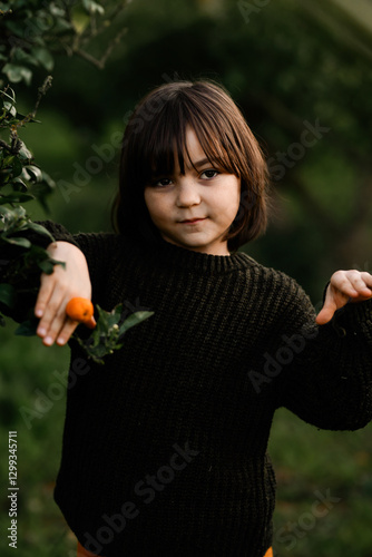 Child in nature holding orange, surrounded by greenery