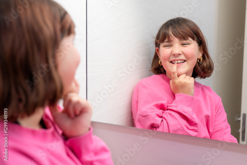 Young girl smiling while checking her milk tooth in mirror photo
