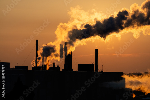 Silhouettes of factory pipe, chimneys at orange sunset with exhaust smoke, steam. Concept ecology, pollution, industry, smog, global warming.