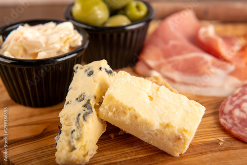 A cheese plate with a variety of cheeses and olives. The cheese is cut into small pieces and arranged on a wooden cutting board