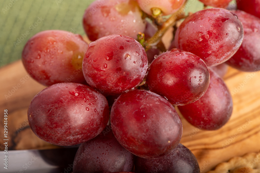 A bunch of grapes are wet and sitting on a wooden cutting board. The grapes are red and shiny, and they are arranged in a cluster. Concept of freshness and abundance, as the grapes are ripe A bunch of grapes are wet and sitting on a wooden cutting board. The grapes are red and shiny, and they are arranged in a cluster. Concept of freshness and abundance, as the grapes are ripe