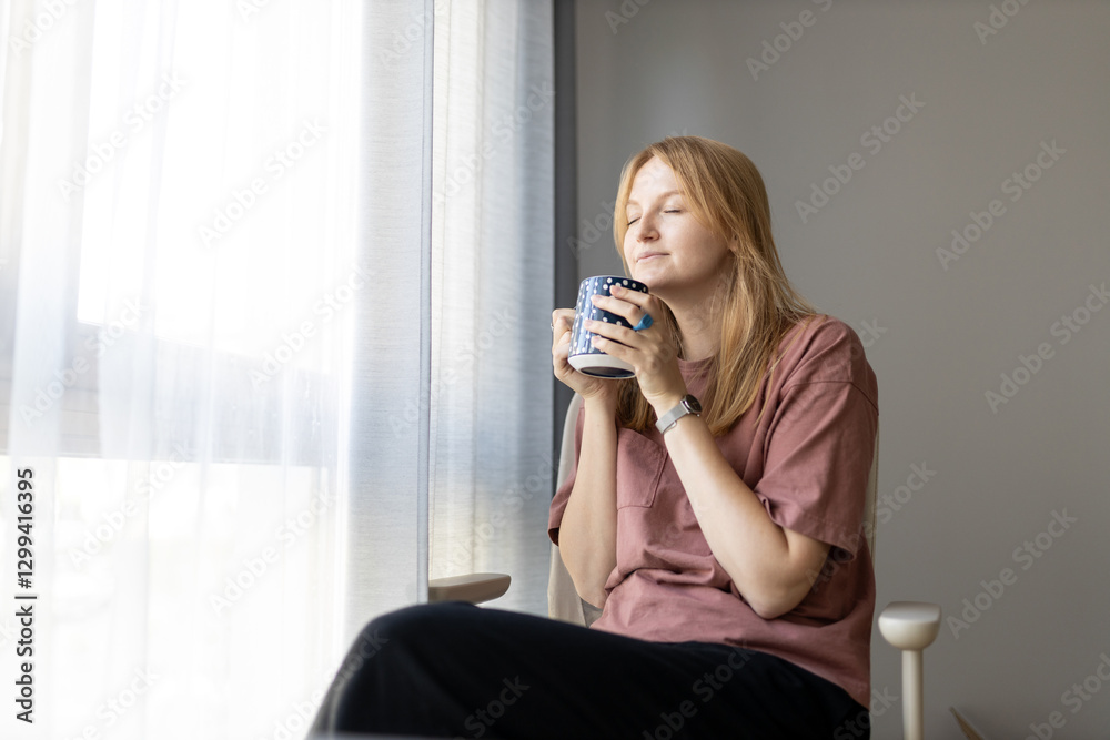Young woman wears t-shirt drink coffee at home, hotel or flat. 30s female rest and spend free spare time in living room indoors. People lounge concept Young woman wears t-shirt drink coffee at home, hotel or flat. 30s female rest and spend free spare time in living room indoors. People lounge concept