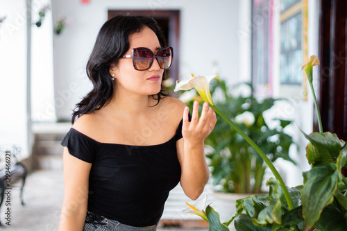 Retrato de mujer joven bonita con gafas belleza acariciando una flor blanca, elegancia y cuidado persona, estilo de vida saludable	