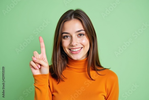 A Smiling Young Caucasian Woman in an Orange Turtleneck Sweater Holding Up Her Index Finger Against a Vibrant Green Background, Signifying Positivity