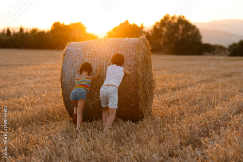 Kids Pushing a Hay Bale in a Sunny Field
