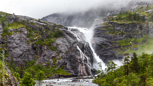 Majestic Waterfall Cascading Down Rocky Cliffs Surrounded by Lush Greenery and Misty Mountains in a Picturesque Natural Landscape Capturing the Essence of Wilderness