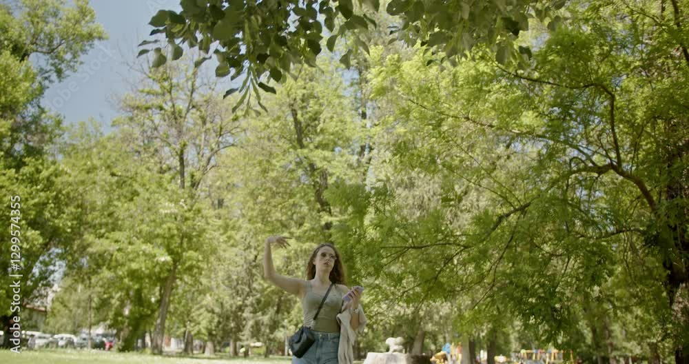 Young woman enjoying a sunny day in the park. She is walking, looking at her phone, and eating a lollipop. Young woman enjoying a sunny day in the park. She is walking, looking at her phone, and eating a lollipop.