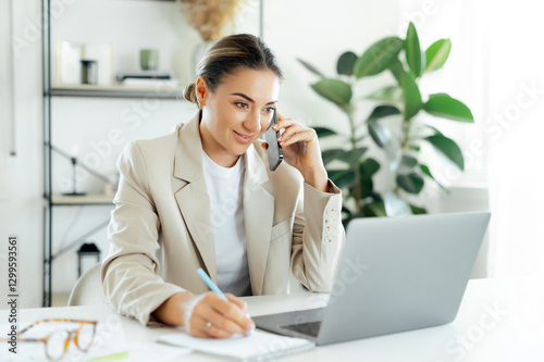 Positive busy businesswoman, office employee in a beige suit is talking on the phone while writing notes at her desk, showing professionalism and effective communication in her work environment