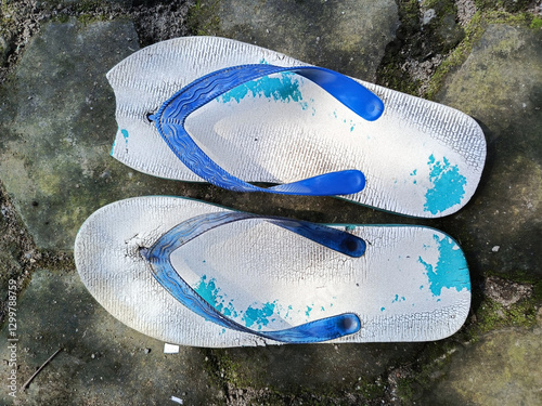 A pair of worn down blue flip flop with broken side.