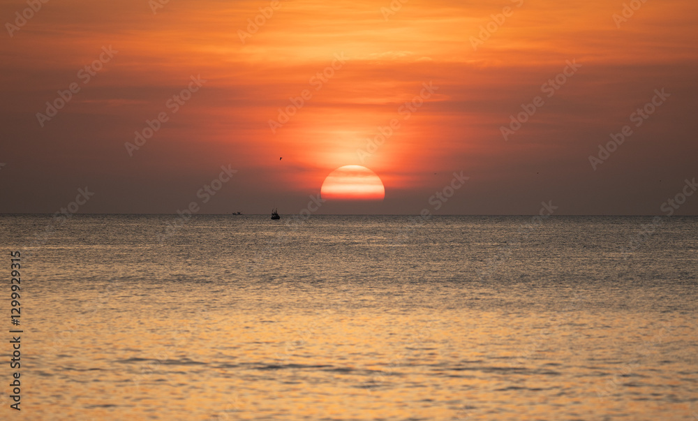 Beautiful sunset over the ocean with golden hues reflecting on the water and small boats in the distance