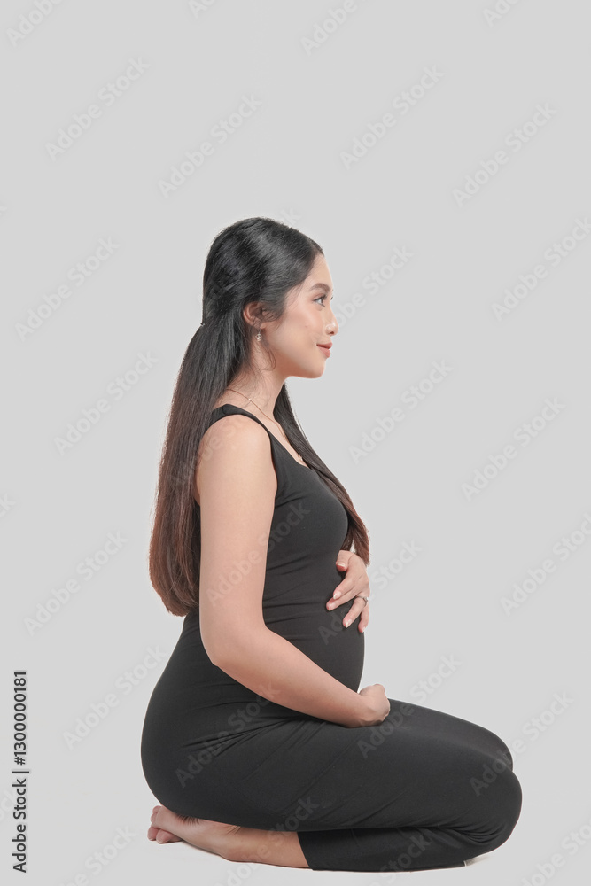 Cheerful pregnant Asian woman sitting on the floor while holding stomach. Cheerful pregnant Asian woman sitting on the floor while holding stomach.