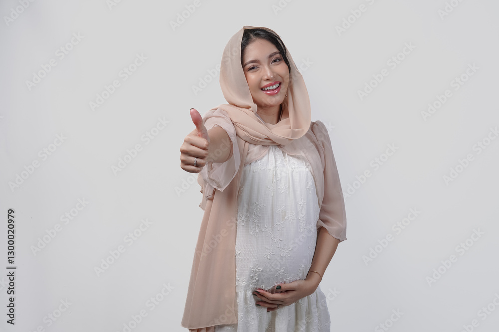 Attractive pregnant Asian woman in white dress and hijab gesturing thumbs up for approval. Attractive pregnant Asian woman in white dress and hijab gesturing thumbs up for approval.