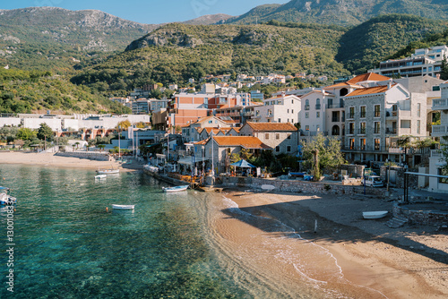 Ancient houses with red roofs with a sandy beach by the sea at the foot of the mountains. Przno, Montenegro