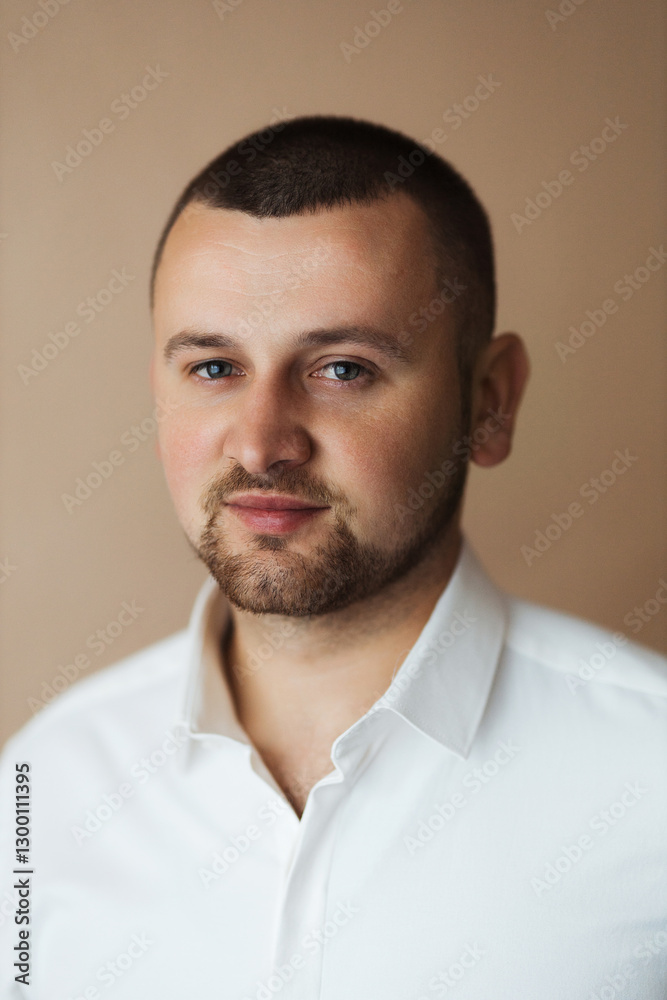 A man with a short haircut and a beard buttons up the buttons on a white shirt. A man with a short haircut and a beard buttons up the buttons on a white shirt.