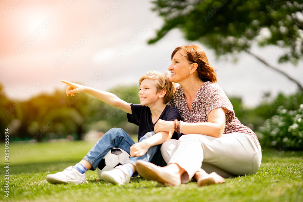 Healthy and happy grandmother sitting on green grass with joyful grandchild at summer park look away. Joyful cuacacian kid take a rest affter exercise with senior woman at garden. Healthy and happy grandmother sitting on green grass with joyful grandchild at summer park look away. Joyful cuacacian kid take a rest affter exercise with senior woman at garden.