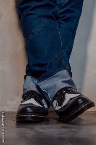 Close up of a man's legs wearing blue jeans paired with two-tone black and white genuine leather brogue shoes. Close up of shiny vintage brogue shoes against a dirty white wall.