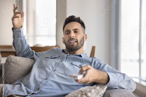 Fotografie Man watching TV with irritated face expression, feels angry due to frequent adve