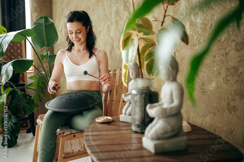 Beautiful young lady playing tank drum on knees at home photo