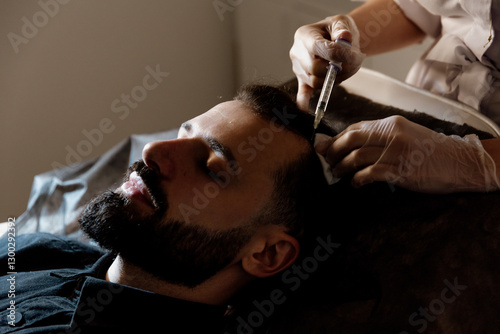 An attractive man receives mesotherapy injections to treat hair loss at the clinic. Injections into the skin and scalp
