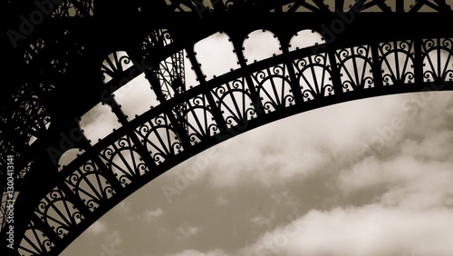 Travelers admire the stunning architecture of the Eiffel Tower, focusing on its ornate ironwork beneath a dramatic sky, evoking a sense of wonder and exploration in Paris