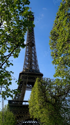 Travelers enjoy a sunny day near the Eiffel Tower, surrounded by lush green trees. The iconic landmark stands tall against a clear blue sky, inviting exploration and adventure