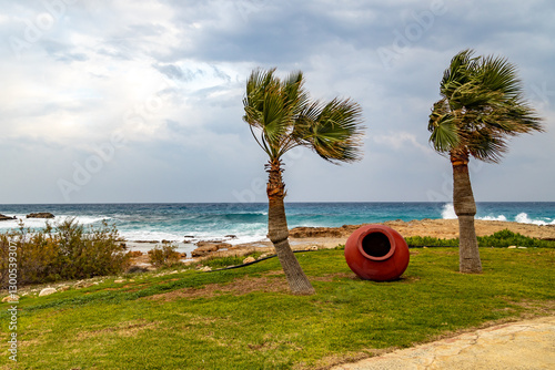 Palm trees and decorative amphora in a strong wind on the beach in stormy weather. January.  Mediterranean, Ayia Napa, Cyprus