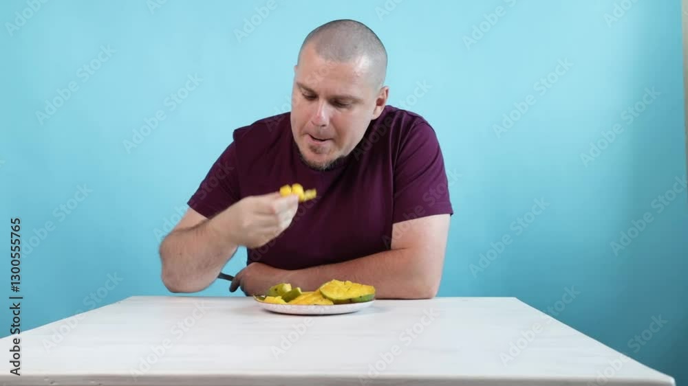 Man Eating Mango Slice on Blue Background, tropical fruit snack for a refreshing moment, healthy lifestyle choice. Man Eating Mango Slice on Blue Background, tropical fruit snack for a refreshing moment, healthy lifestyle choice.
