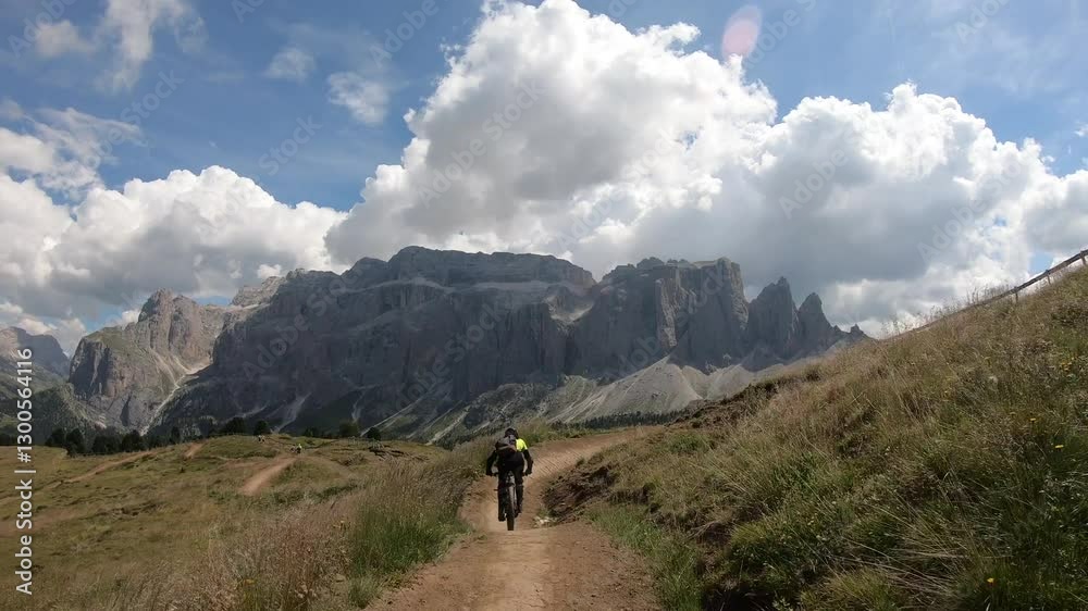 A cyclist pedals uphill under a vast blue sky with dramatic clouds, conquering the rugged terrain of the Dolomite mountains. A cyclist pedals uphill under a vast blue sky with dramatic clouds, conquering the rugged terrain of the Dolomite mountains.