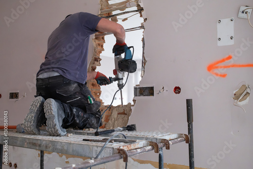 A construction worker on scaffolding demolishes a wall in a building with a hammer drill. photo