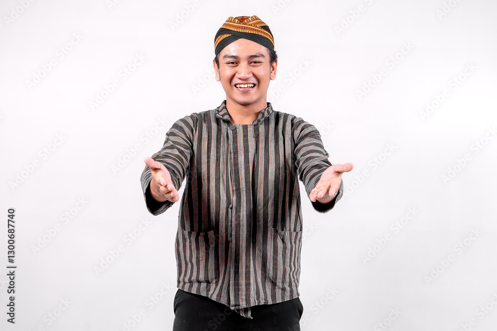 A young Indonesian man wearing traditional lurik attire smiles warmly while extending his arms in a welcoming gesture against a neutral background, showcasing cultural pride and friendliness. A young Indonesian man wearing traditional lurik attire smiles warmly while extending his arms in a welcoming gesture against a neutral background, showcasing cultural pride and friendliness.