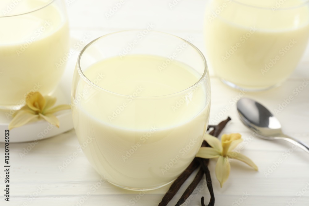 Delicious vanilla milk in glasses, pods and flowers on white wooden table, closeup Delicious vanilla milk in glasses, pods and flowers on white wooden table, closeup