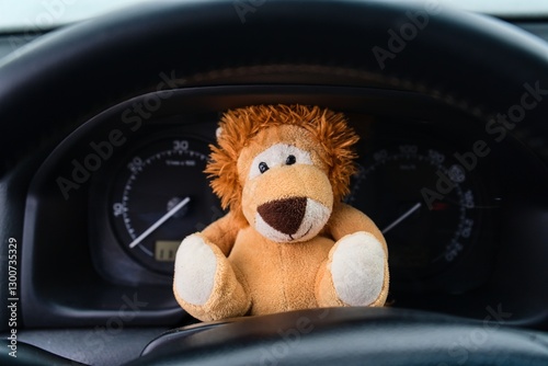 Plush Lion Toy Sitting Behind Car Steering Wheel with Speedometers in Background