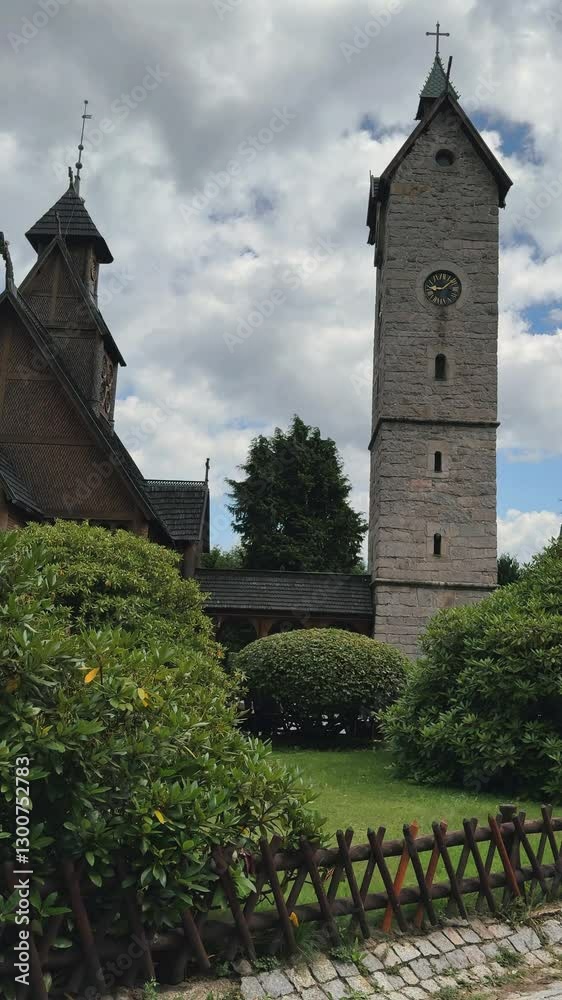 Historic clock tower and stone church surrounded by lush greenery on a cloudy day Historic clock tower and stone church surrounded by lush greenery on a cloudy day