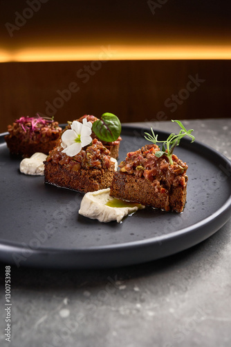 Gourmet appetizer, rye bread pieces with flavorful toppings, garnished creatively, served elegantly on black plate, fine dining concept