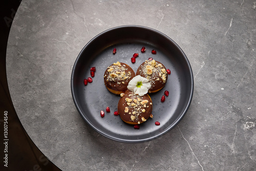 Obraz na płótnie Chocolate-covered donuts garnished with nuts and pomegranate seeds on dark plate, floral decoration, dessert presentation concept w salonie