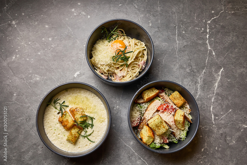 Gourmet pasta, salad, and creamy soup in bowls on marble surface, showcasing elegant dining dish concept