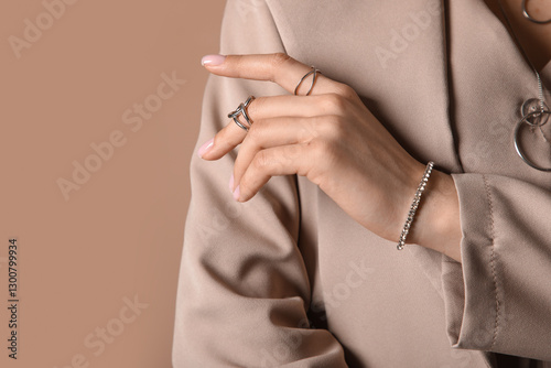 Pretty young woman in stylish blazer with silver rings, bracelet and necklace on beige background, closeup