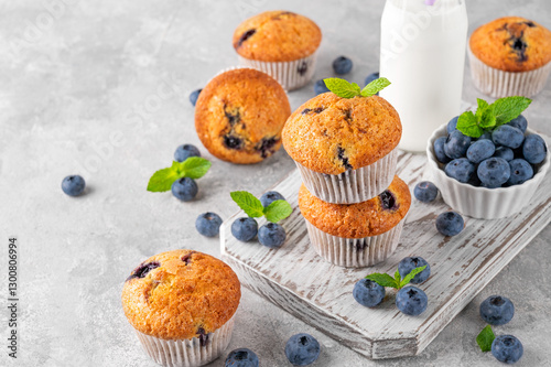 Delicious blueberry muffins on a wooden board on a gray concrete background with a bottle of milk, fresh berries and mint leaves.